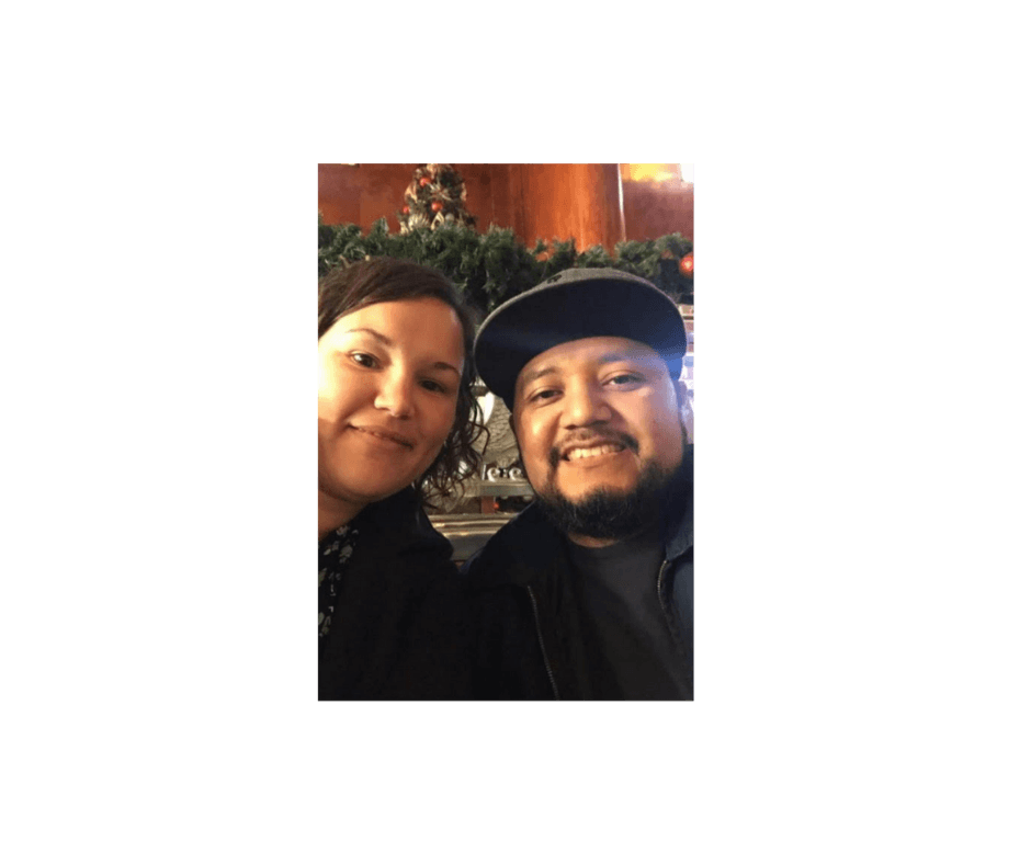 Smiling man and woman posing for a selfie in front of festive indoor Christmas decorations.